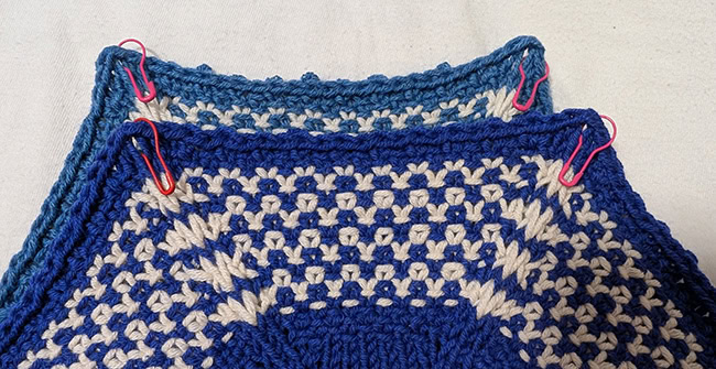 The top of two hexagons laid over each other, right sides facing. There are stitch markers in the top two corners of each of them, showing where to put them.